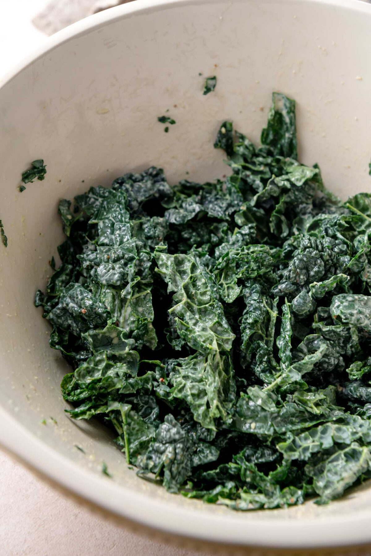 Chopped kale leaves massaged with dressing in a mixing bowl, showing softened texture and glossy coating.