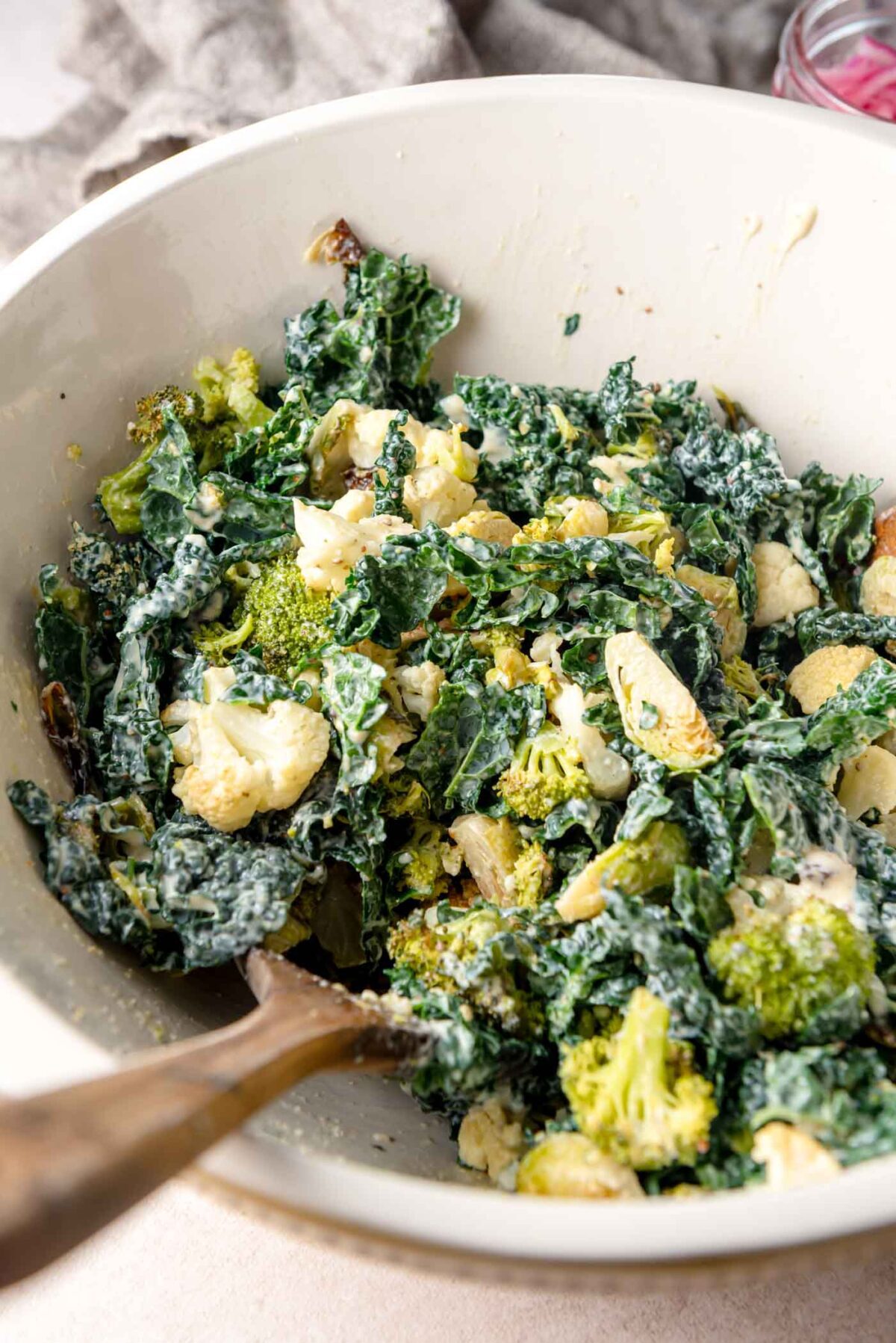 Large mixing bowl of kale Caesar salad with roasted broccoli and cauliflower tossed in creamy dressing.