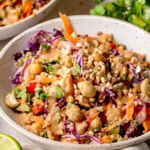 Detailed close-up of quinoa salad with red cabbage, carrots, edamame, chickpeas, herbs, and peanut sauce coating everything.