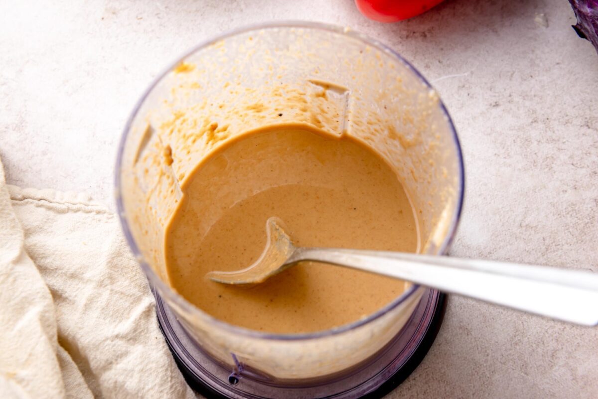 Peanut sauce blended in a food processor until smooth and creamy, with a spoon showing the thick, pourable texture.