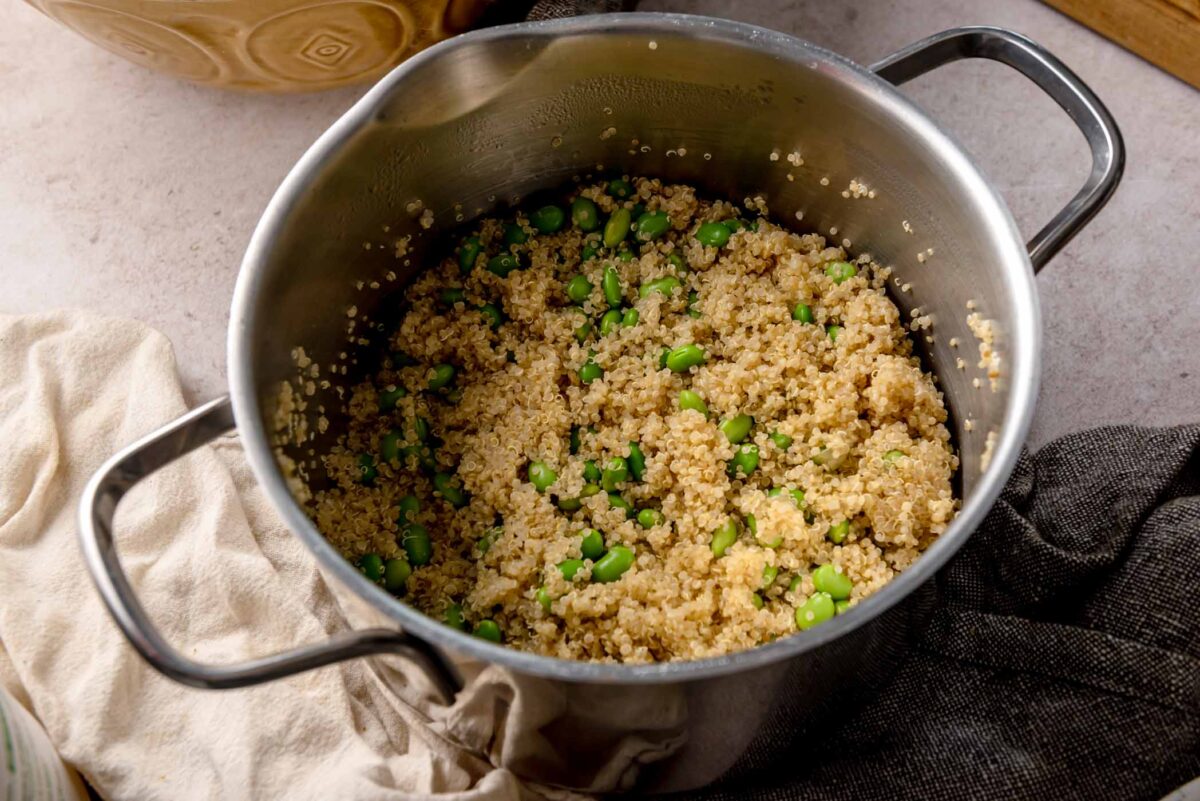 Cooked quinoa with edamame in a saucepan, light and fluffy grains mixed with bright green soybeans.