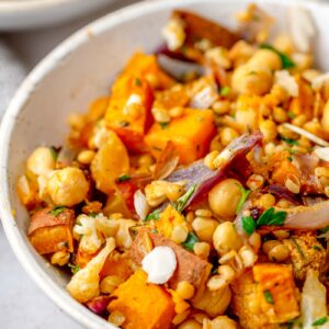 Close-up of a bowl with roasted sweet potato, cauliflower, chickpeas, lentils and chopped herbs.