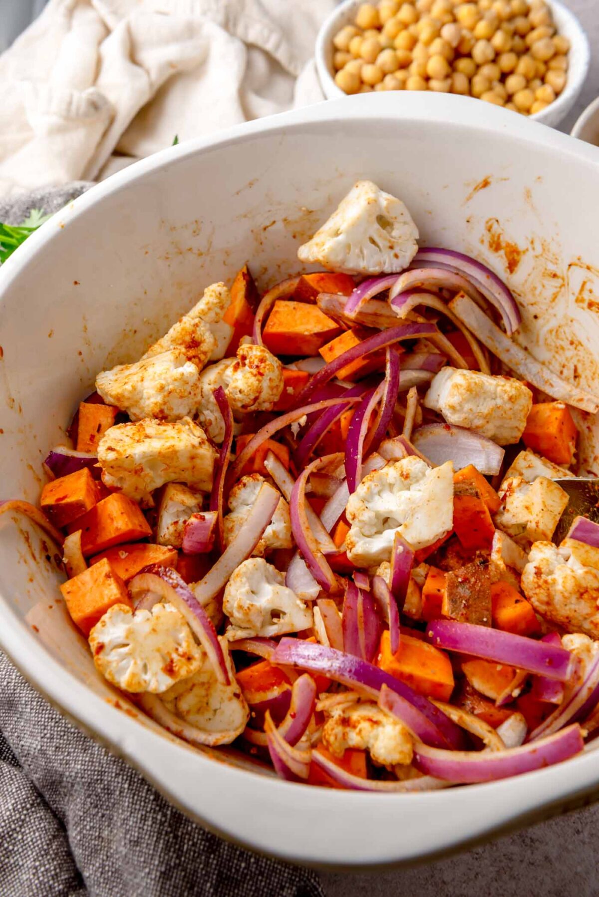 Cauliflower, sweet potato and red onion coated in seasoning in a mixing bowl.