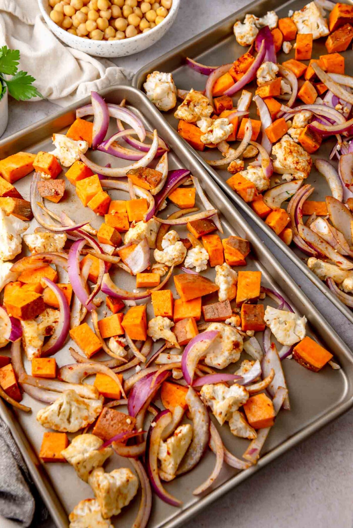 Cauliflower, sweet potato and red onion spread on a baking sheet before roasting.