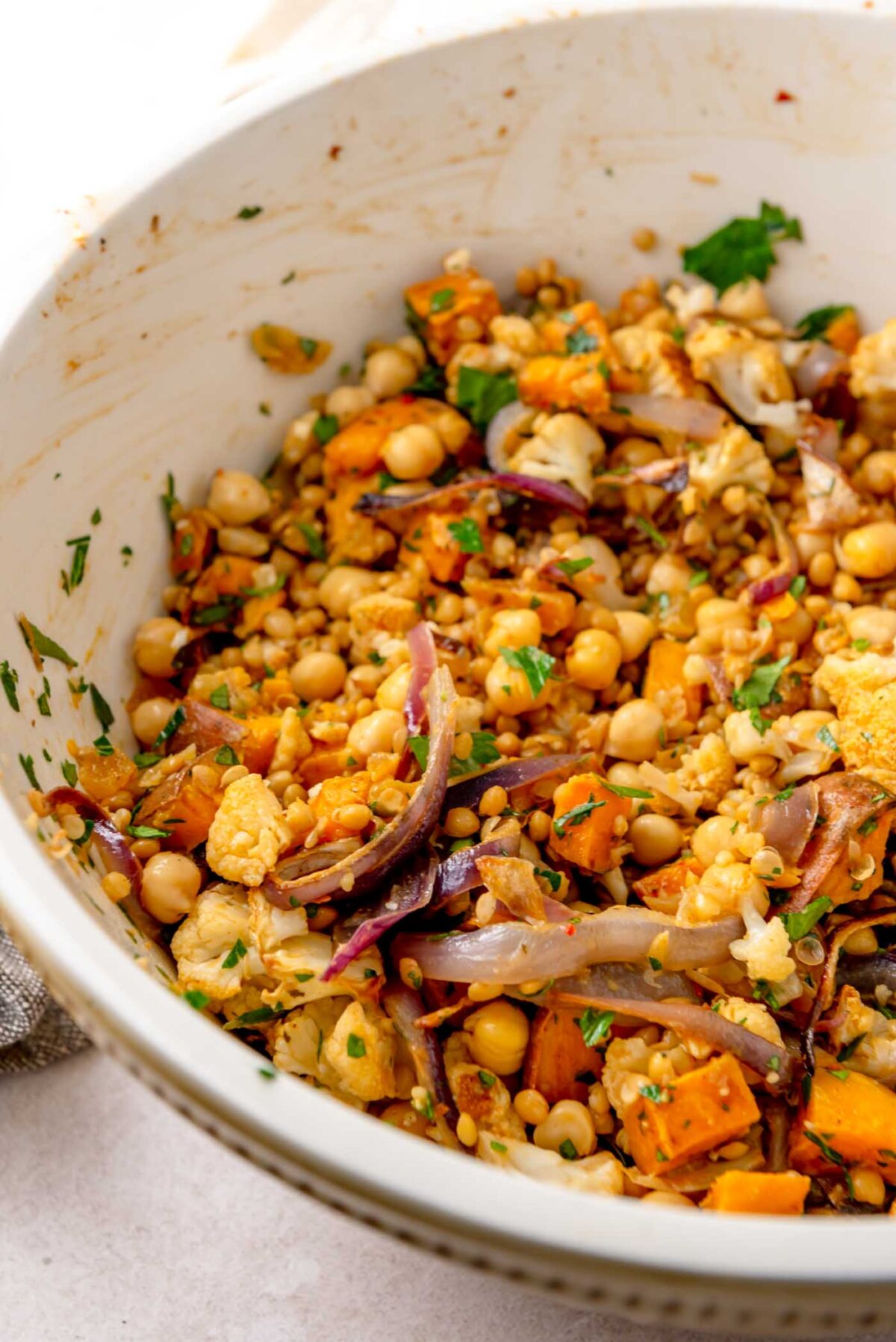 Roasted vegetables, chickpeas, lentils and herbs tossed together in a large mixing bowl.