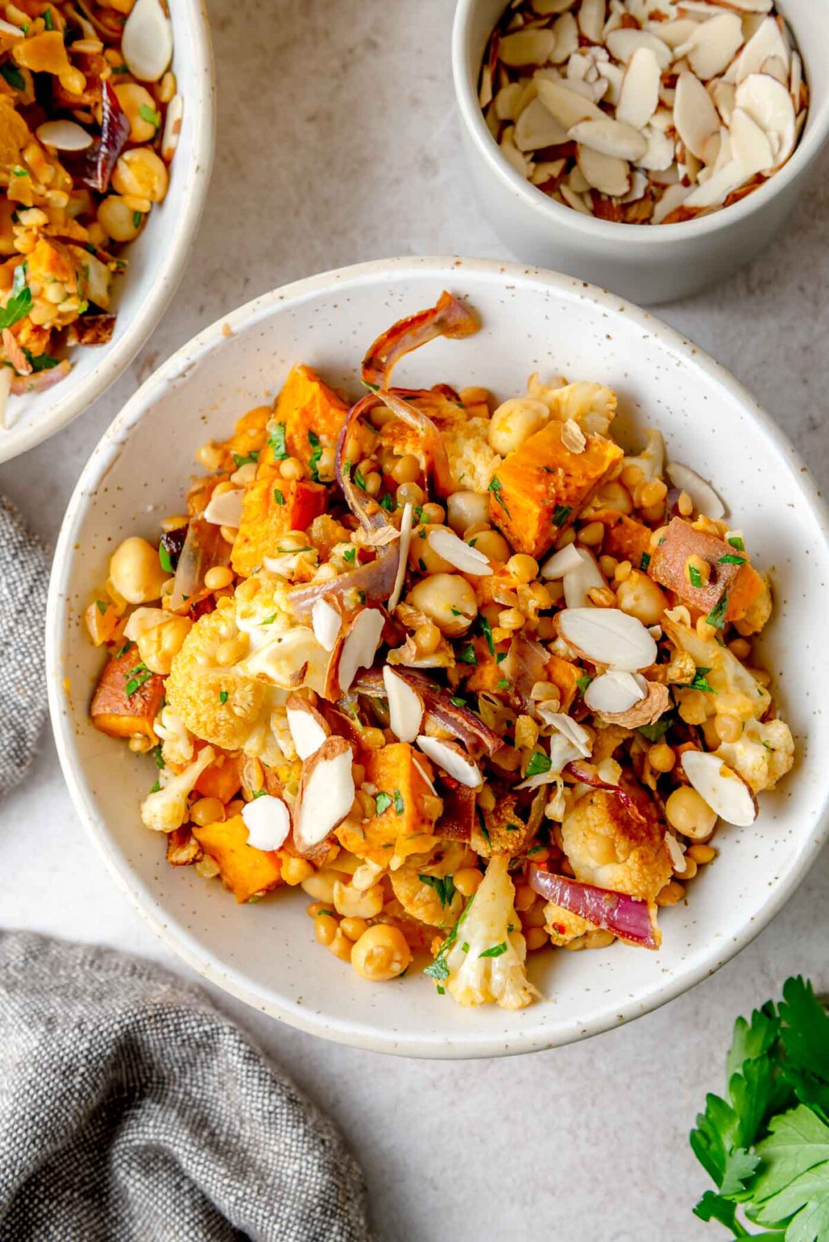 Roasted cauliflower, sweet potato and chickpea salad topped with sliced almonds in a bowl.