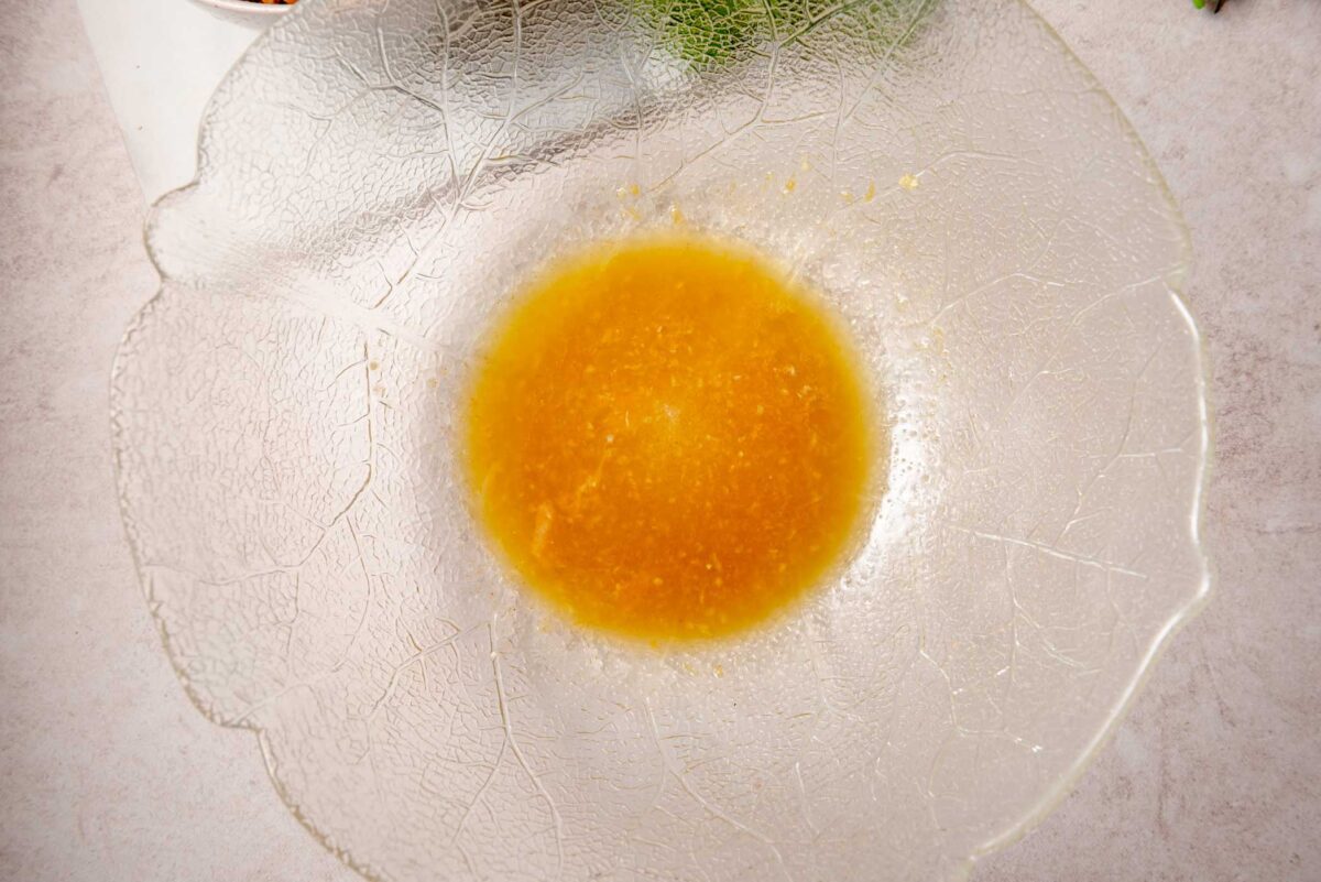 Lemon dressing made with olive oil, lemon juice, lemon zest, maple syrup, garlic and cumin in a glass bowl.