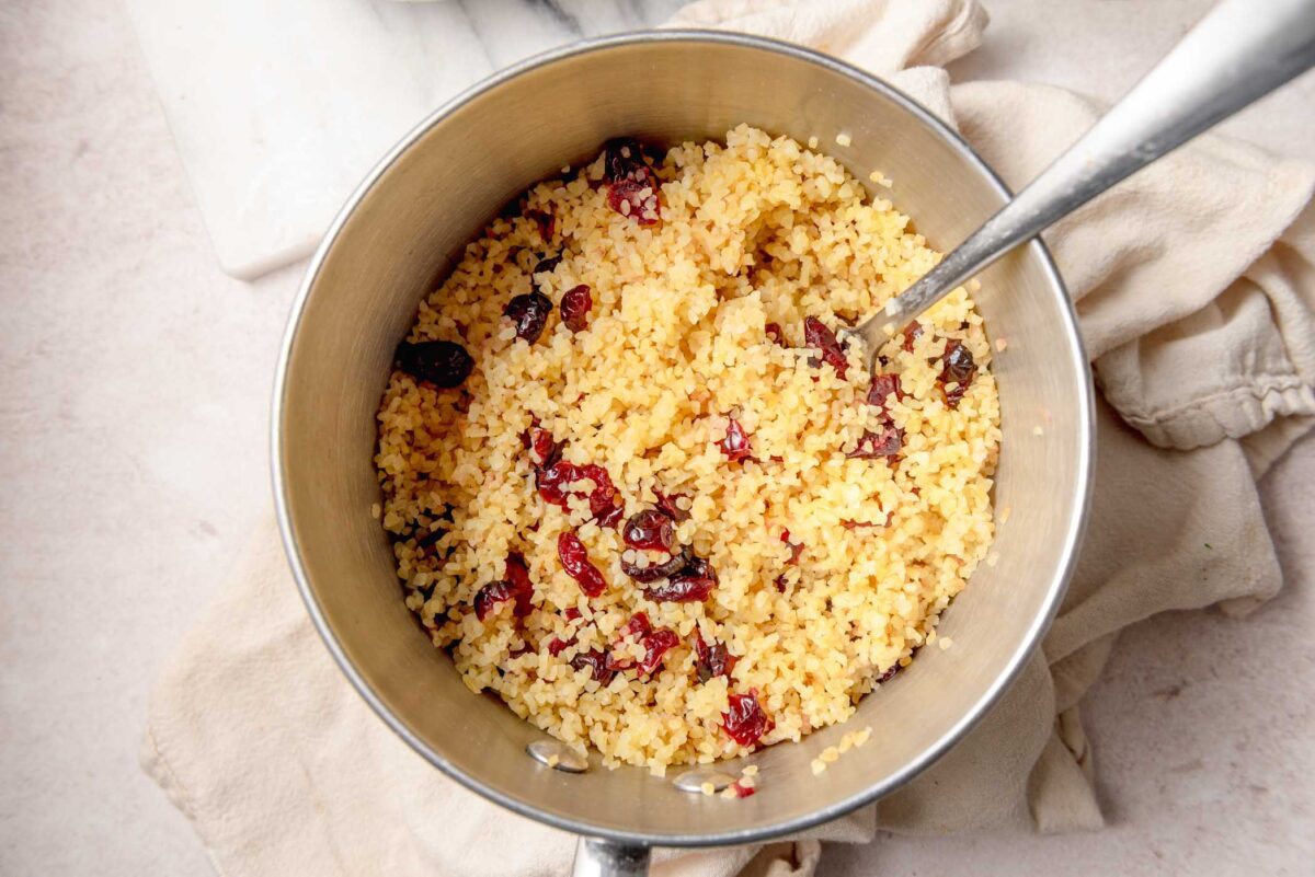 Cooked bulgur mixed with dried cranberries in a small stainless steel pot.