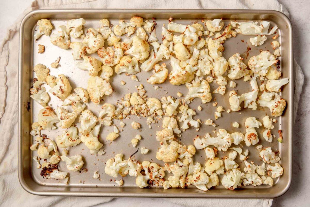 Roasted cauliflower florets with golden-brown edges arranged on a baking sheet.