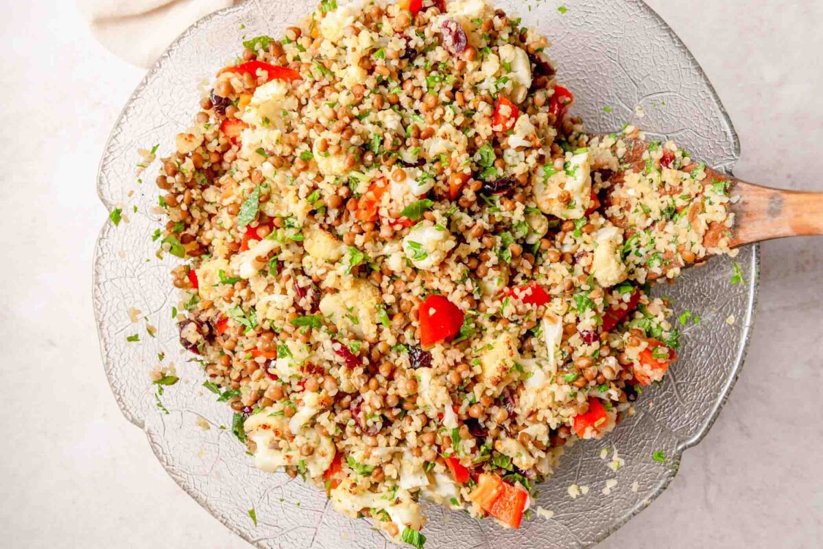 Bulgur salad with lentils, roasted cauliflower, red bell pepper, dried cranberries, parsley and mint served on a large glass platter.