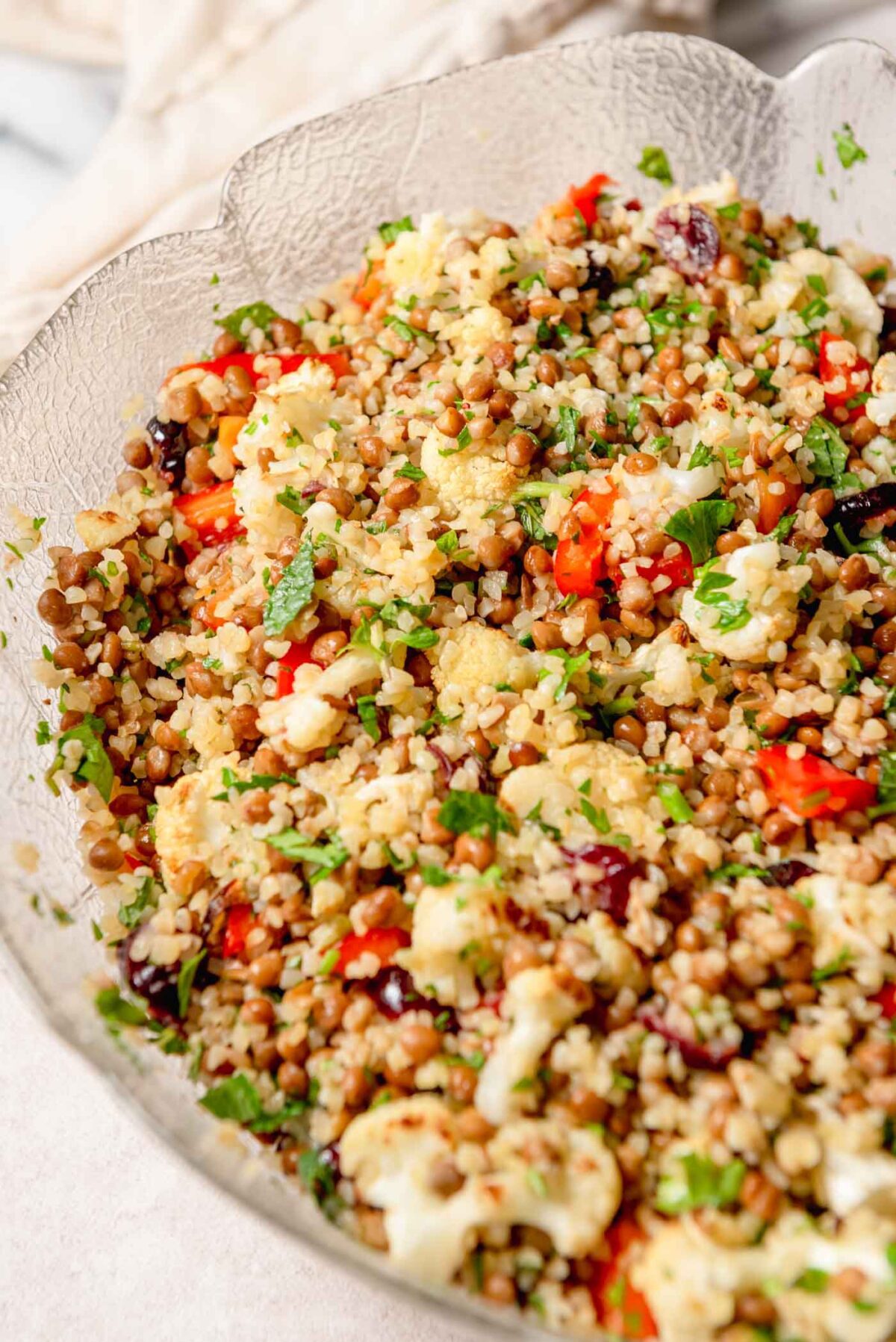 Bulgur lentil salad with roasted cauliflower, red bell pepper, dried cranberries, parsley and mint served on a glass platter.